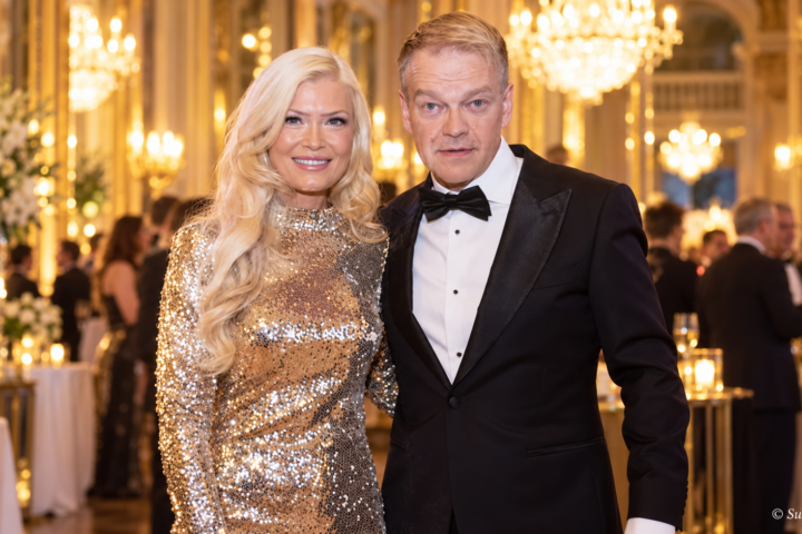 Kurre Westerlund ja Jenna Välikangas poseeraavat yhdessä juhlavassa tilaisuudessa. Välikankaalla on kimaltava kultainen iltapuku ja Westerlundilla musta smokki. Taustalla näkyvät näyttävät kattokruunut ja juhlavieraat.