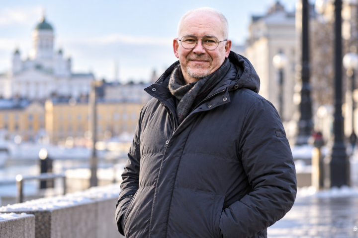 Mika Saarelainen poseeraa talvisessa Helsingin kaupunkimaisemassa lämpimään takkiin ja huiviin pukeutuneena.