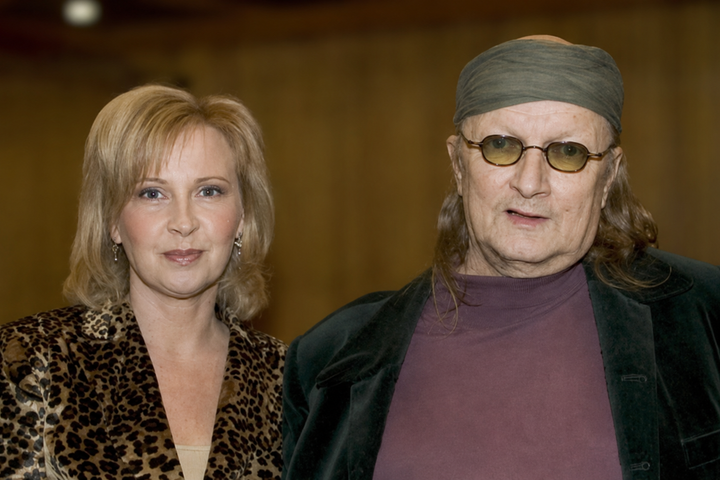 Sari Leskinen ja Juice Leskinen seisovat vierekkäin sisätiloissa sumeutettua puista taustaa vasten.