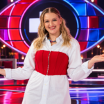 Jenni Poikelus poseeraa Big Brother Suomen uutena juontajana värikkäällä studiolla, taustallaan ohjelman tunnusomainen silmälogo ja näyttävät punasiniset lavavalot.