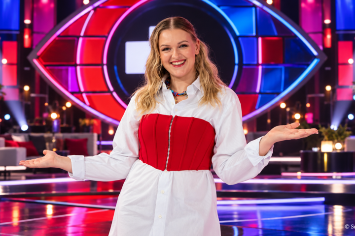 Jenni Poikelus poseeraa Big Brother Suomen uutena juontajana värikkäällä studiolla, taustallaan ohjelman tunnusomainen silmälogo ja näyttävät punasiniset lavavalot.