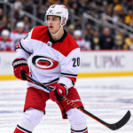 Carolina Hurricanesin peliasua käyttävä jääkiekkoilija Sebastian Aho luistelee kiekon kanssa NHL-ottelun aikana.