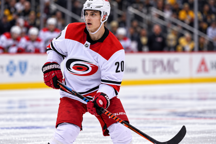 Carolina Hurricanesin peliasua käyttävä jääkiekkoilija Sebastian Aho luistelee kiekon kanssa NHL-ottelun aikana.